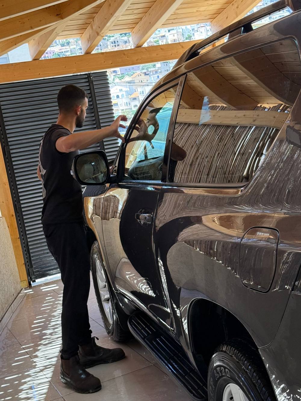 A detailer cleaning a car's glass by hand at DODO Detailing in Maghar